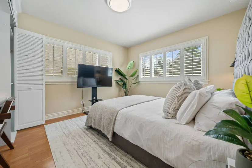 Chambre confortable avec un grand lit, télévision et lumière naturelle provenant de plusieurs fenêtres
