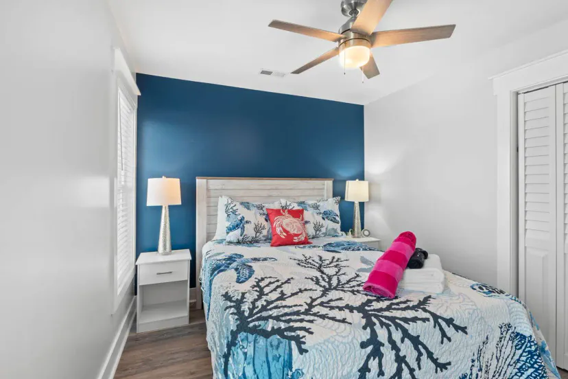 Cozy bedroom featuring a blue accent wall, a queen bed with coral-themed bedding, and bedside lamps