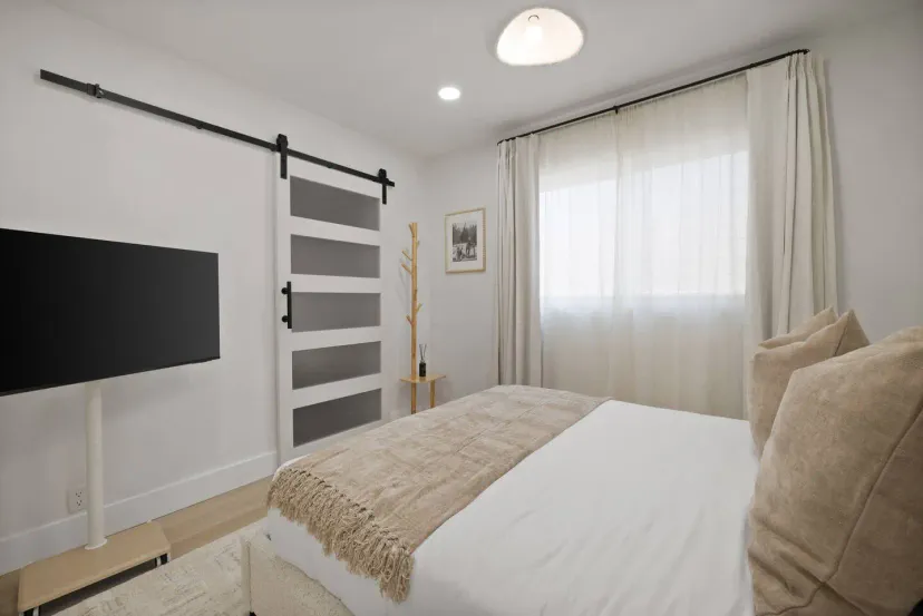 Cozy guest bedroom with a large bed, TV, and natural light from the window