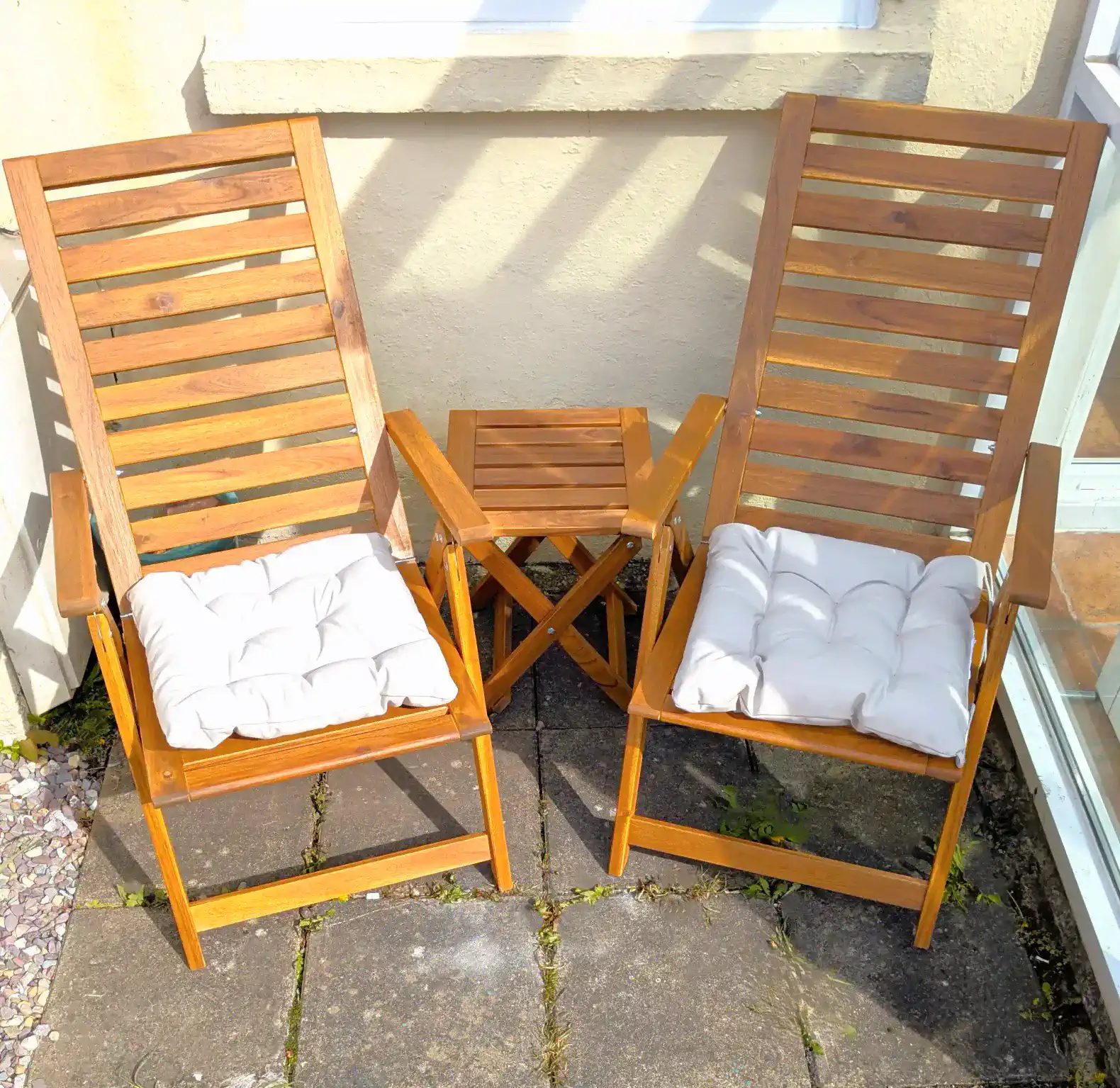Two wooden lounge chairs with cushions beside a small folding table on a patio