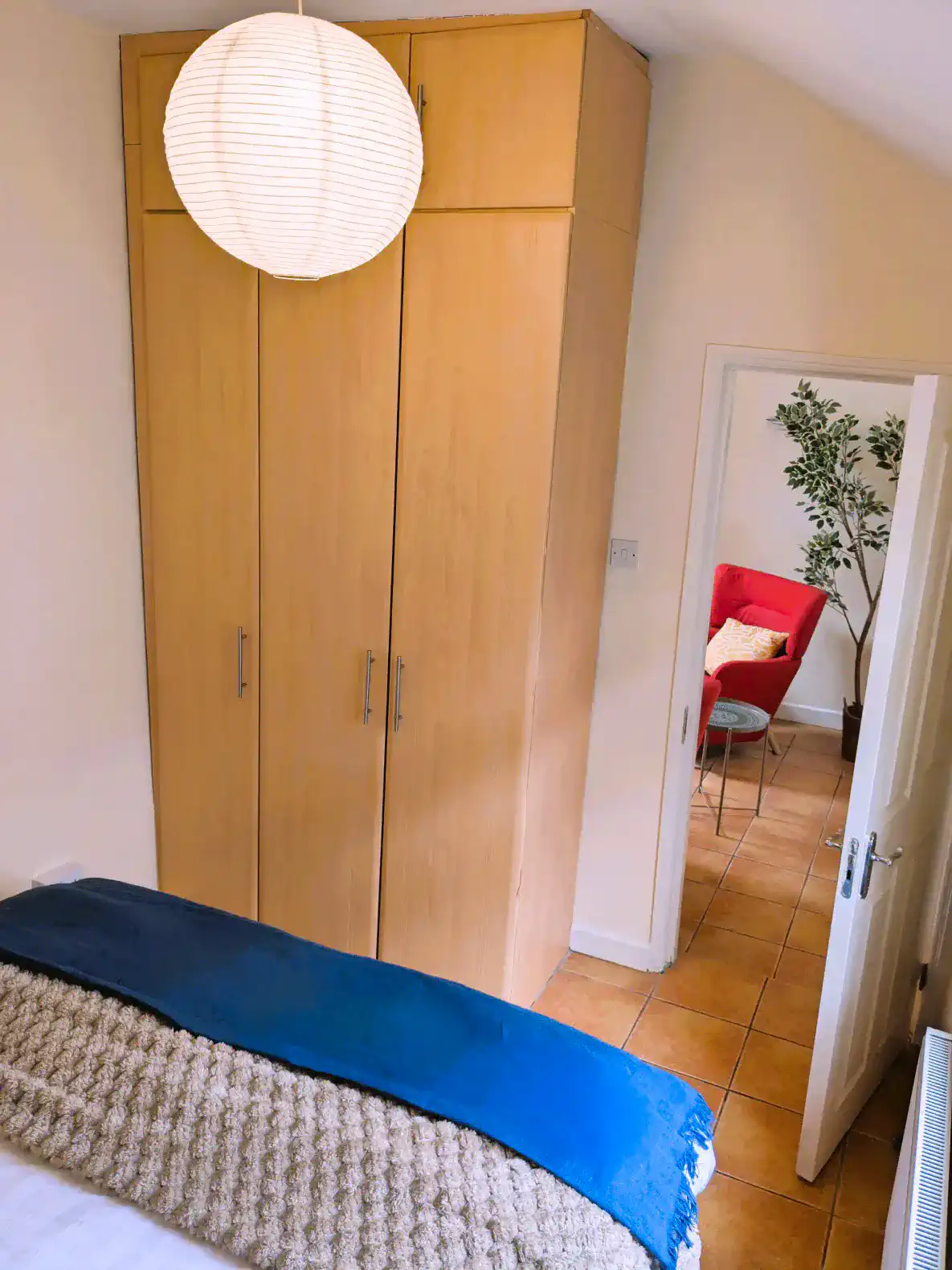 Cozy bedroom with wooden wardrobe and a view of a red chair in the background
