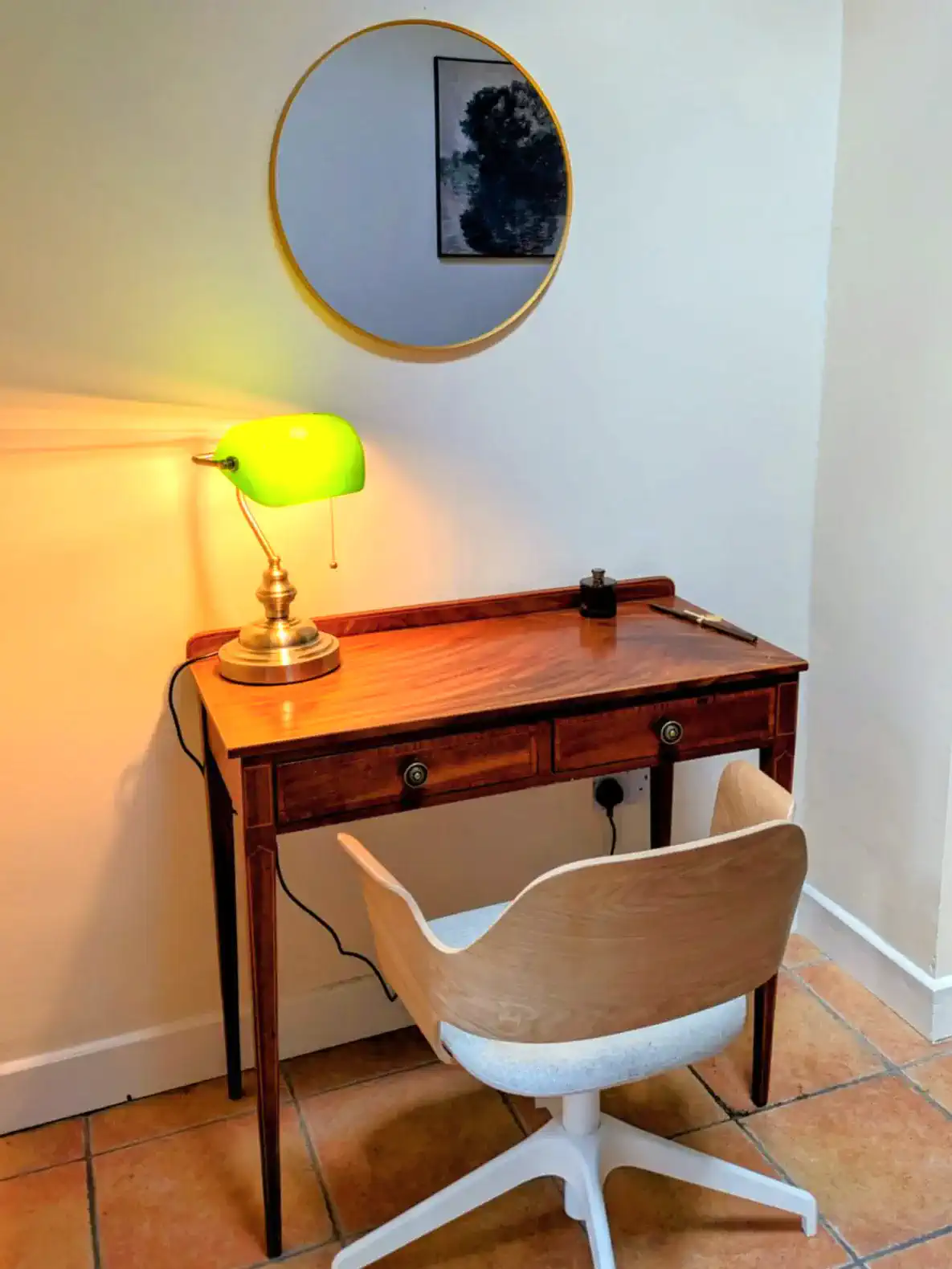 Cozy workspace with a wooden desk, green lamp, and round mirror