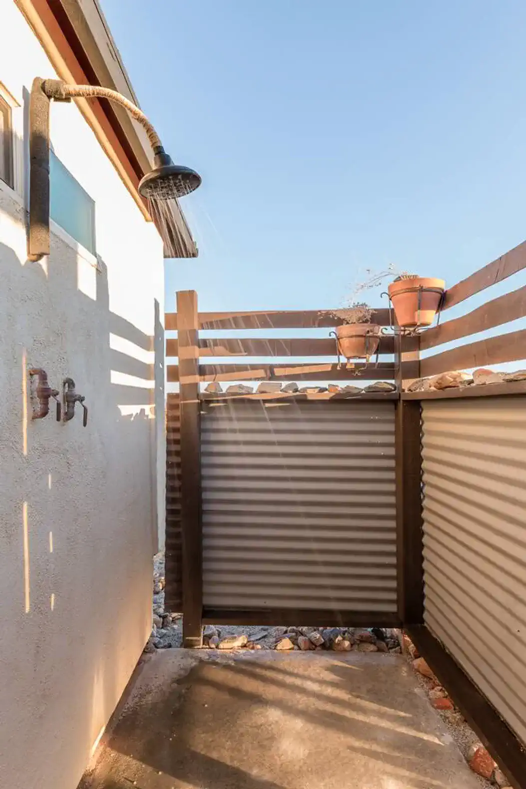 Outdoor shower area with wooden privacy slats and potted plants