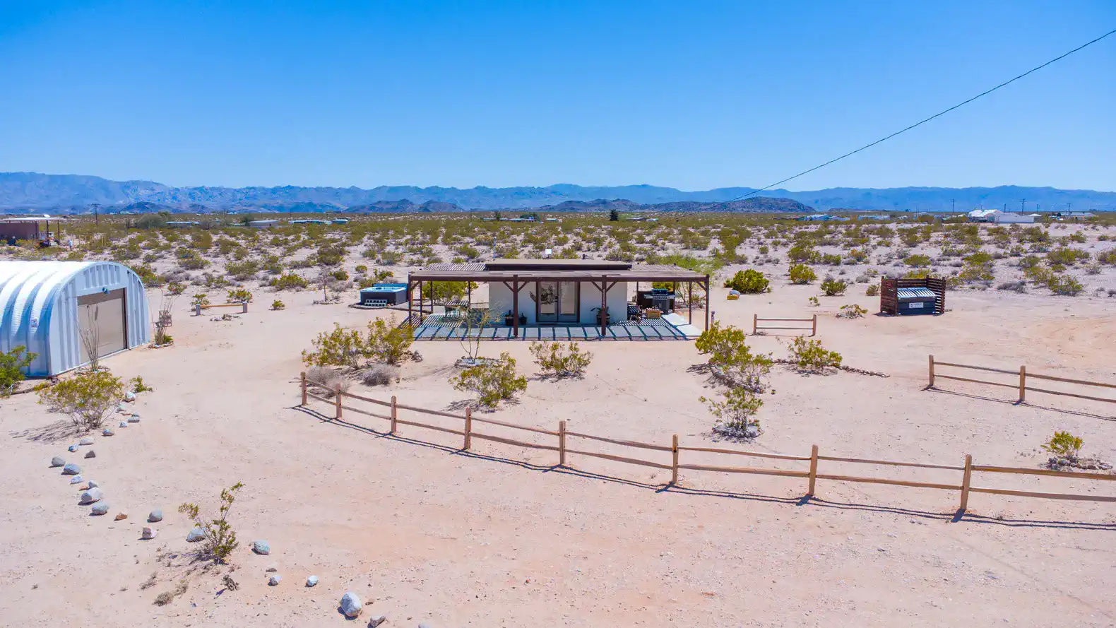 Desert landscape with a modern house surrounded by sparse vegetation and mountains in the background