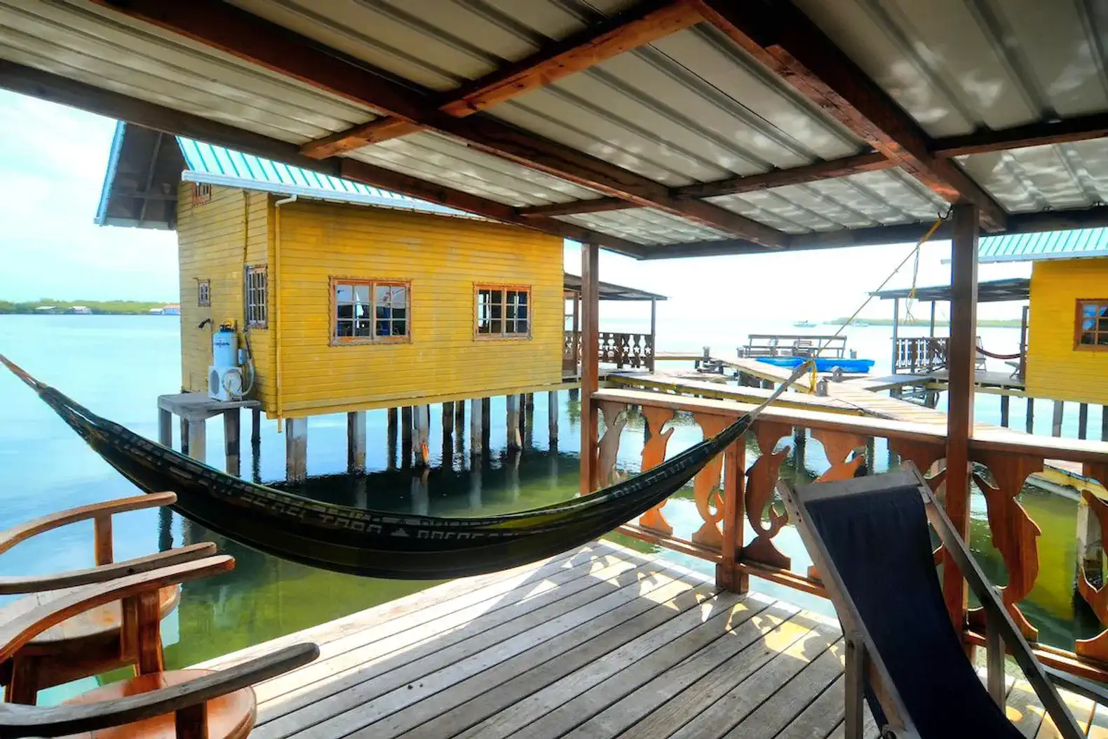 Hammock on a wooden deck overlooking the water with a yellow bungalow in the background
