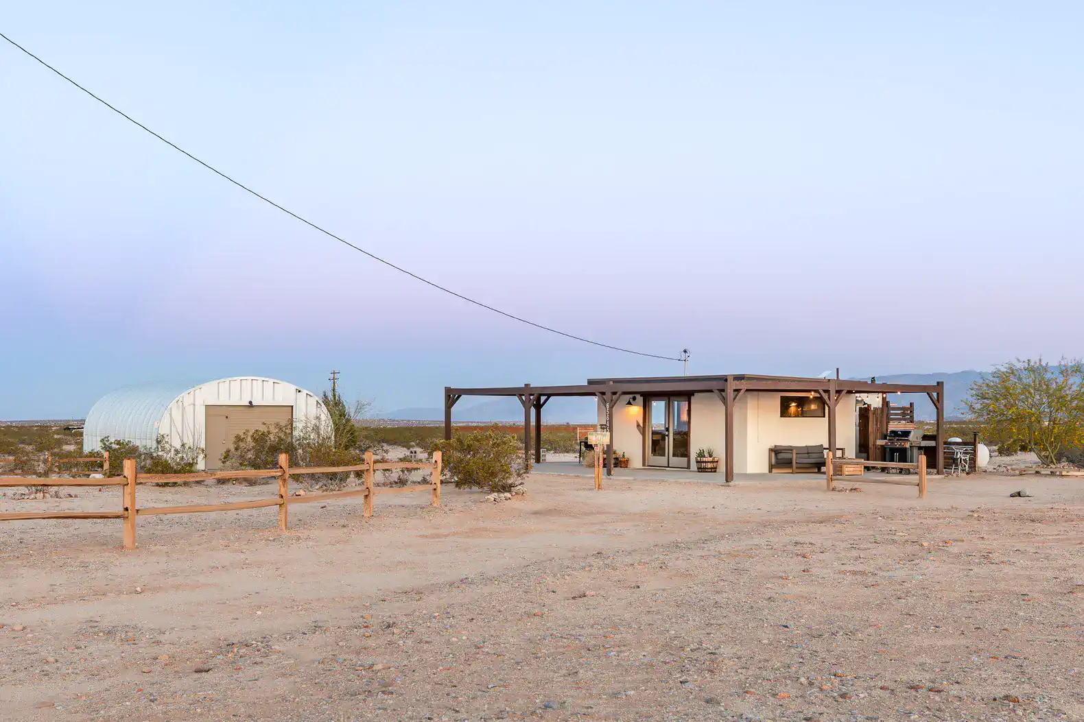 Desert landscape featuring a modern cabin with a covered porch and a nearby storage structure