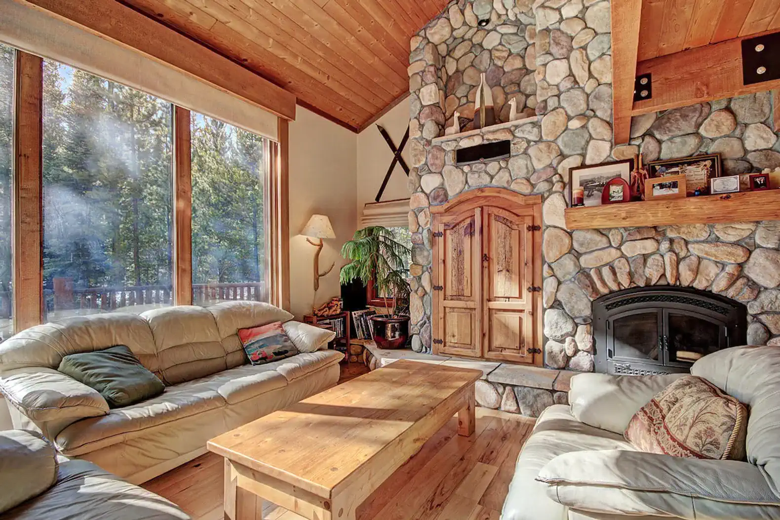 Cozy living room with stone fireplace and large windows overlooking the forest
