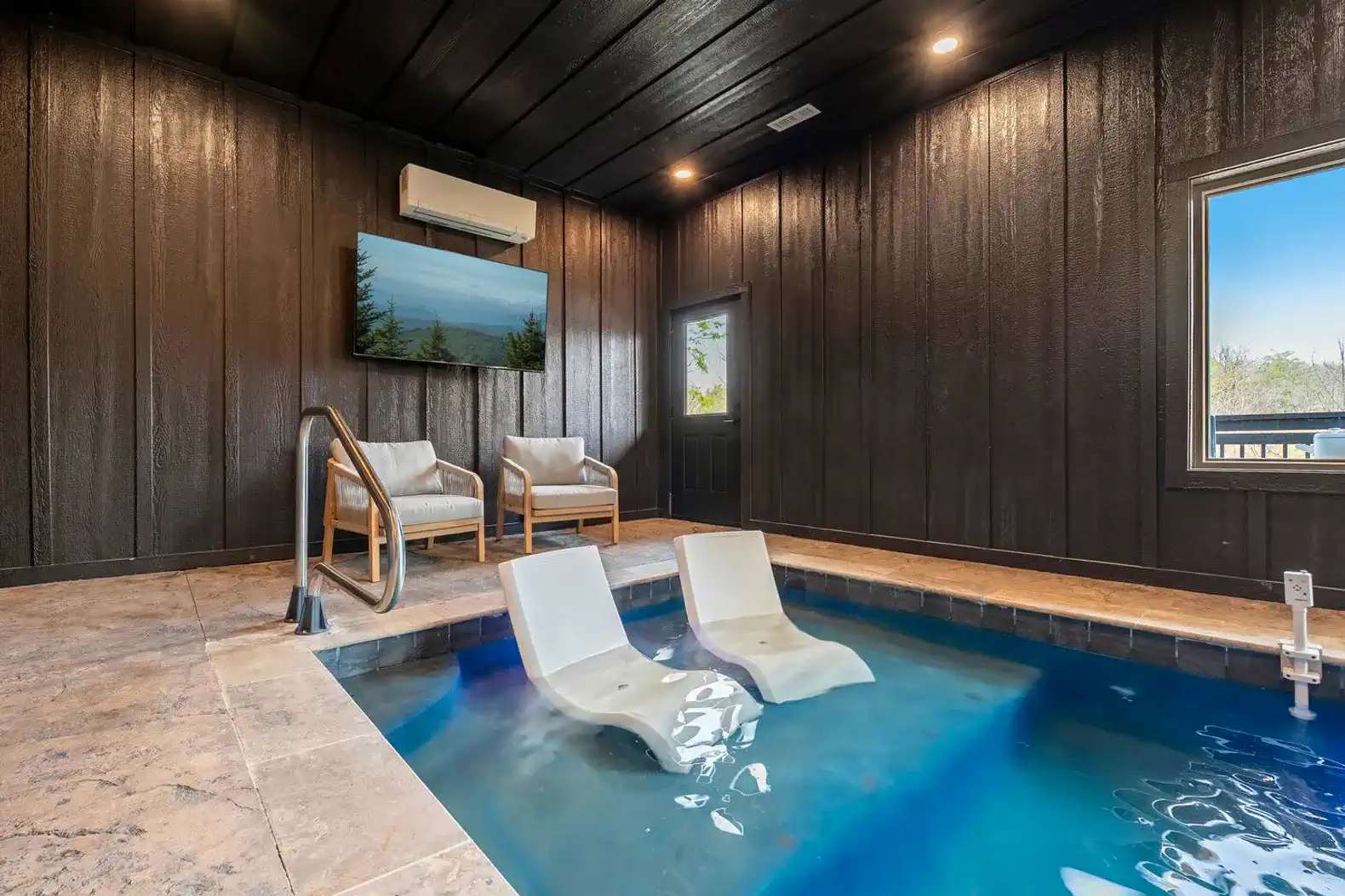 Indoor pool area with seating and a TV, featuring a dark wood ceiling