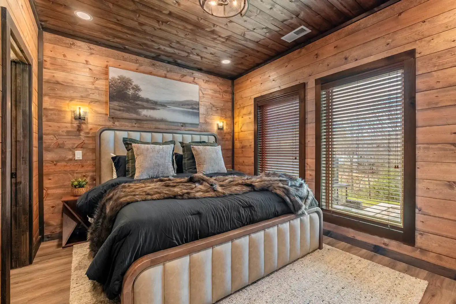 Cozy master bedroom with wooden walls, large windows, and plush bedding