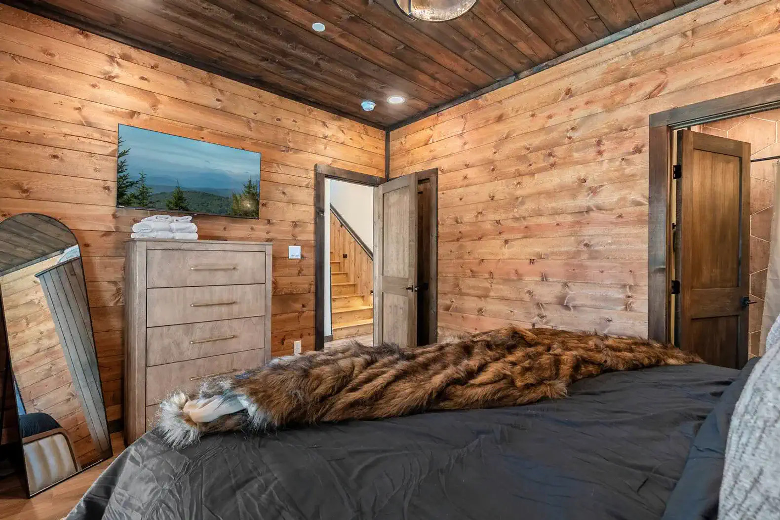 Cozy bedroom with wooden walls, a dresser, and a view of the outdoors