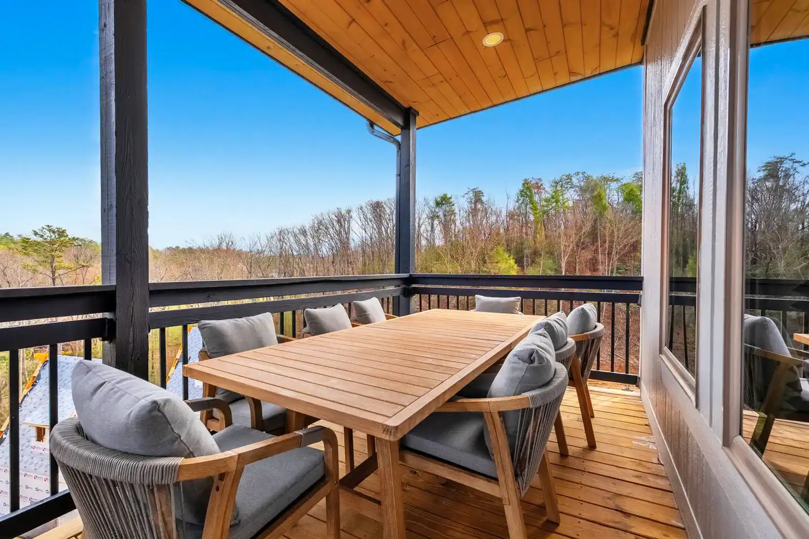 Spacious outdoor dining area with wooden table and comfortable chairs overlooking trees