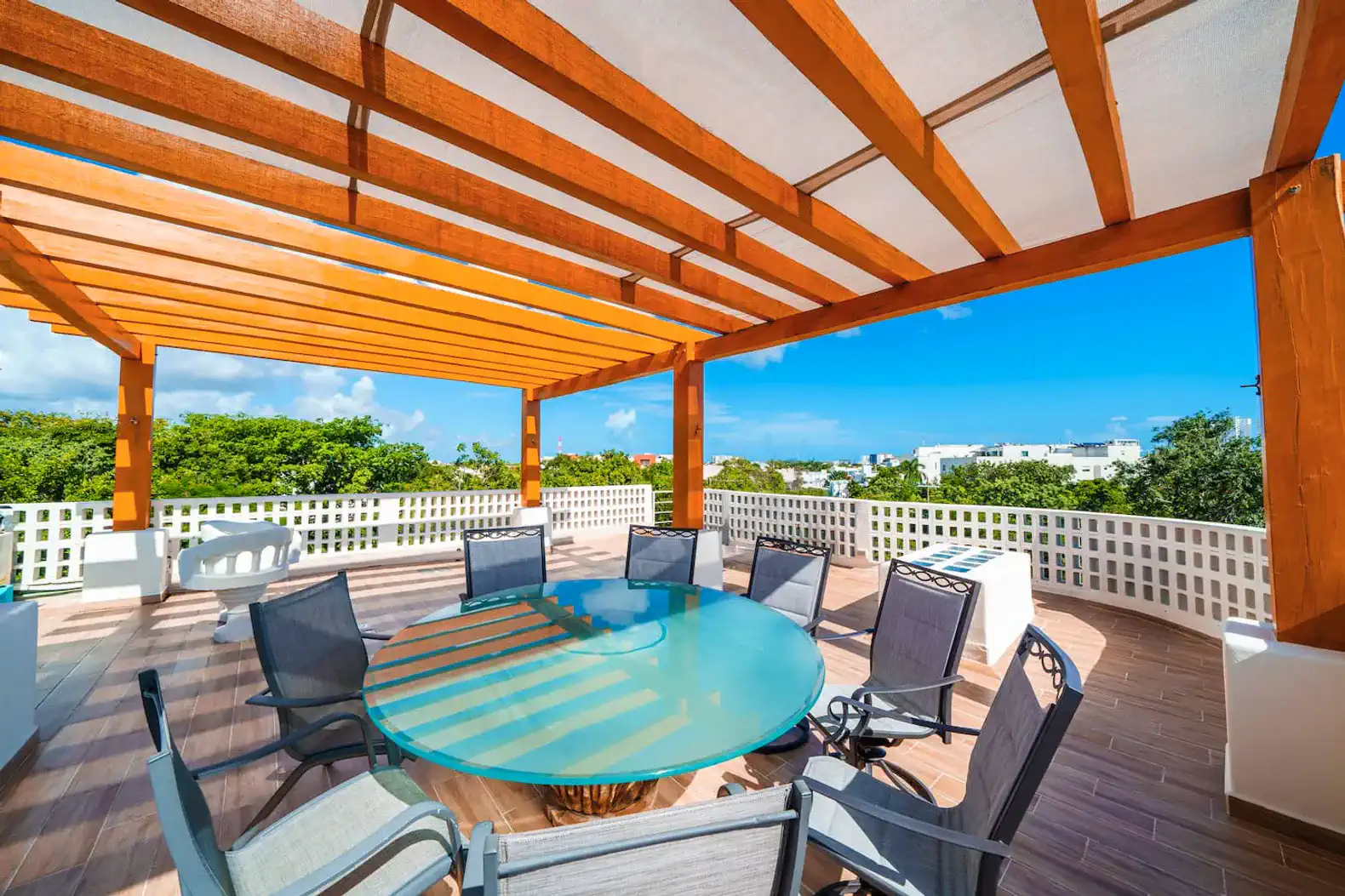 Spacious outdoor terrace with a round glass table and comfortable seating under a wooden pergola
