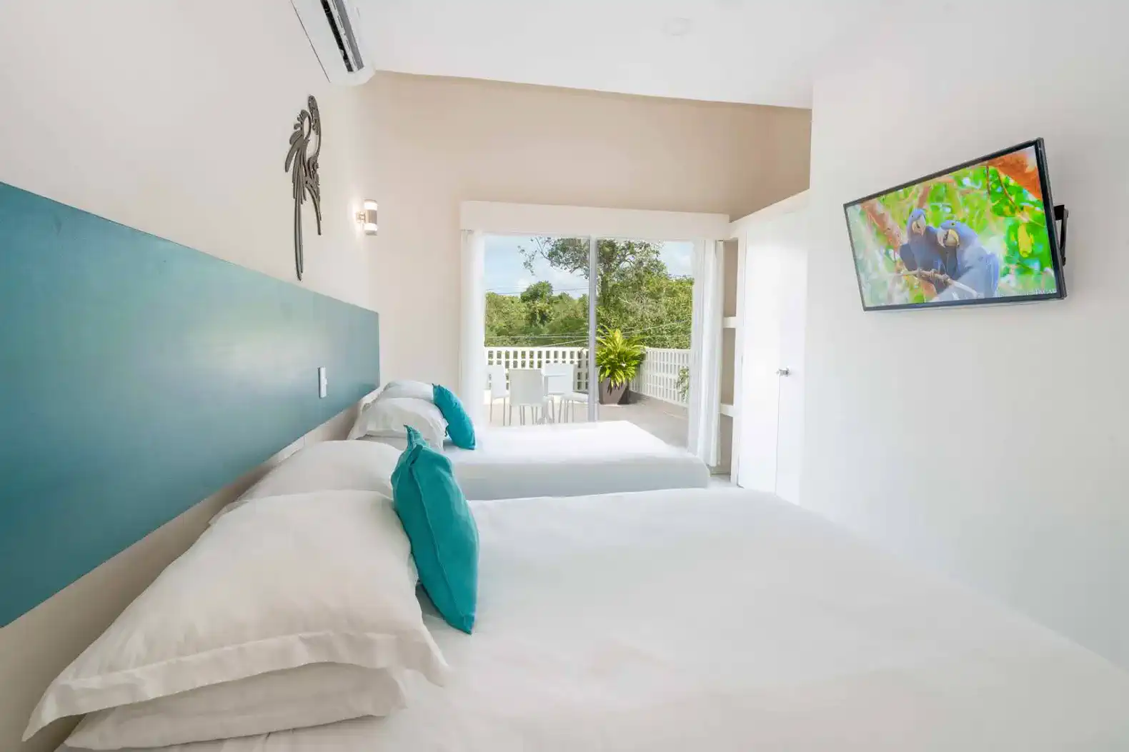 Bright guest bedroom with two beds and balcony access overlooking greenery