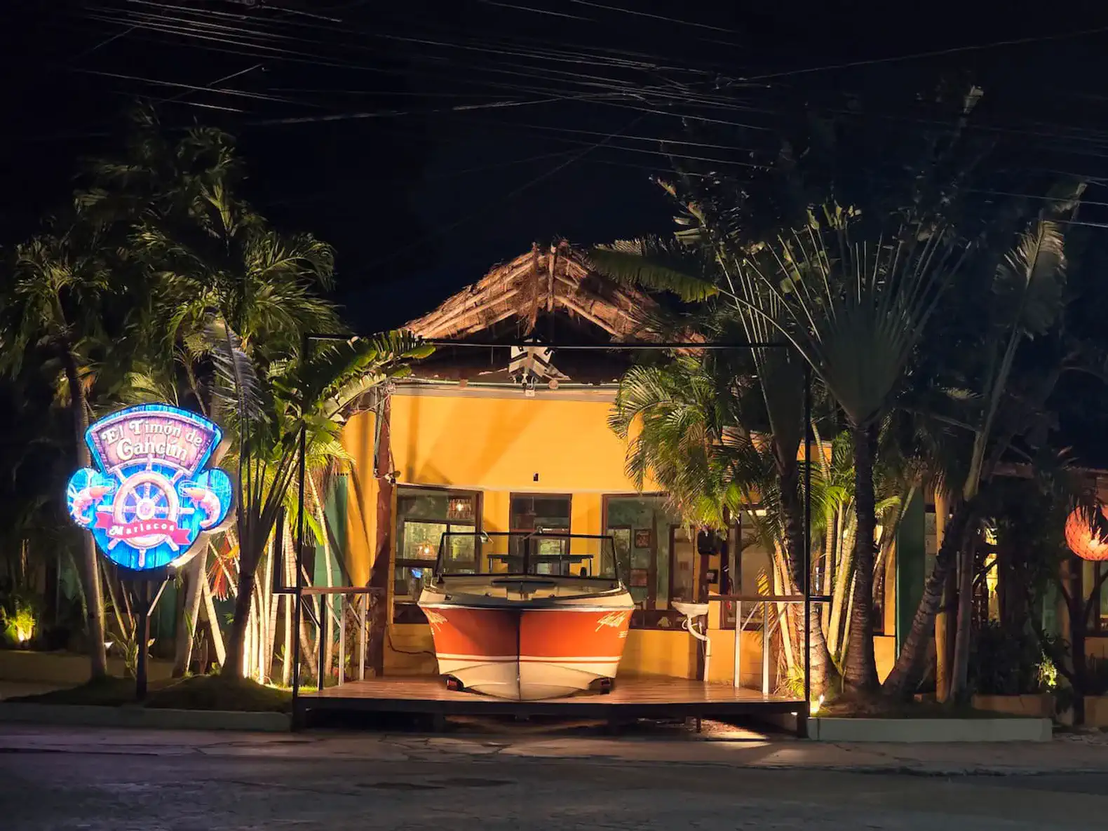 Vibrant entrance with tropical plants and a boat display under night lighting