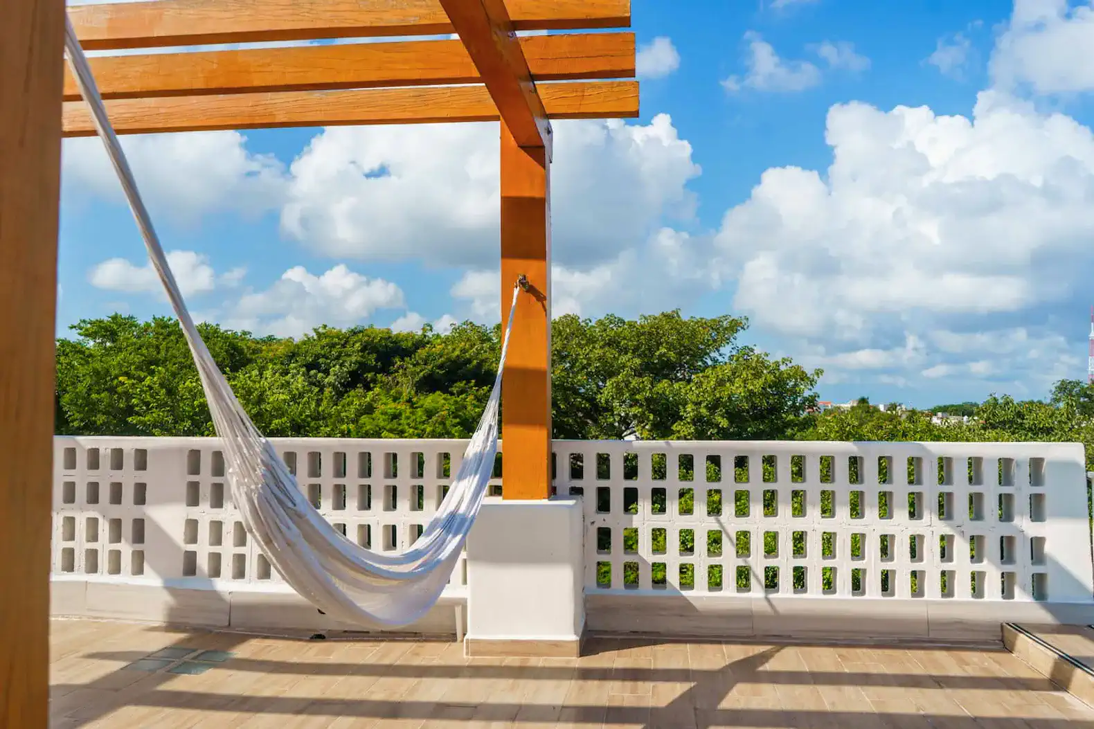Relaxing hammock under a wooden pergola with a view of lush greenery and blue sky