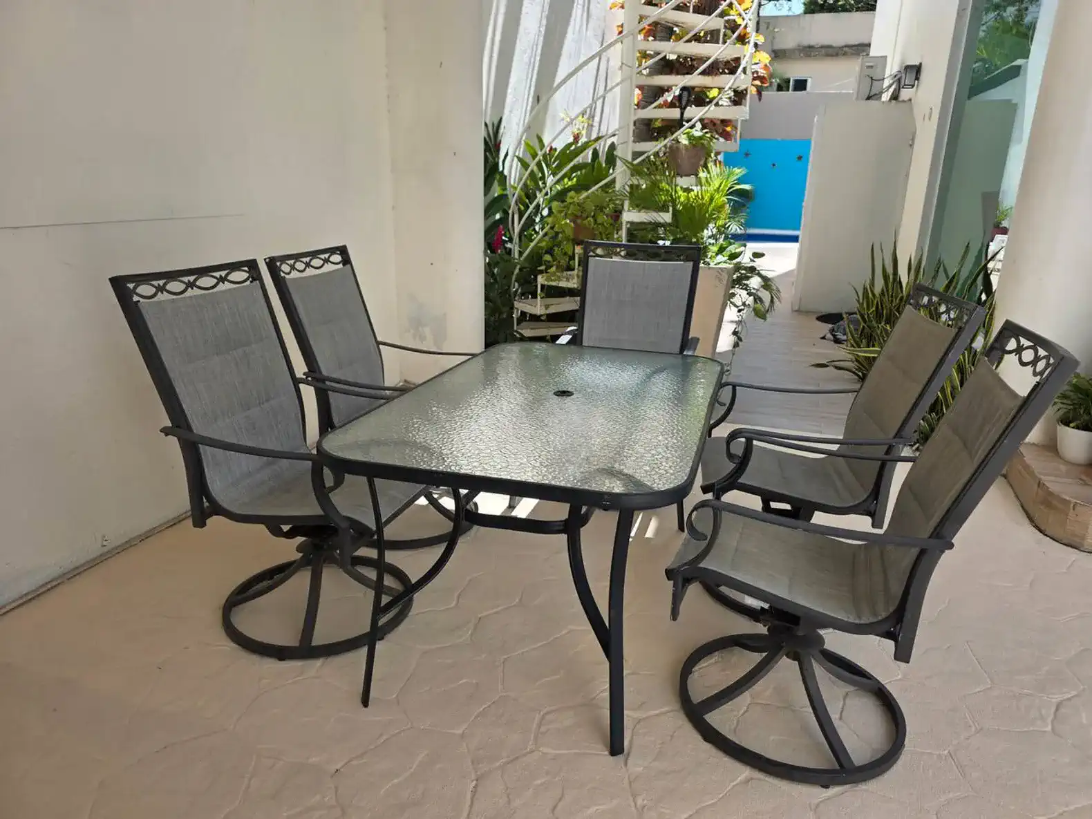 Outdoor dining set with glass table and swivel chairs surrounded by greenery