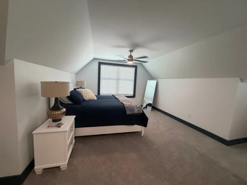 Spacious bedroom with a king-size bed, modern lamps, and a large mirror under sloped ceilings