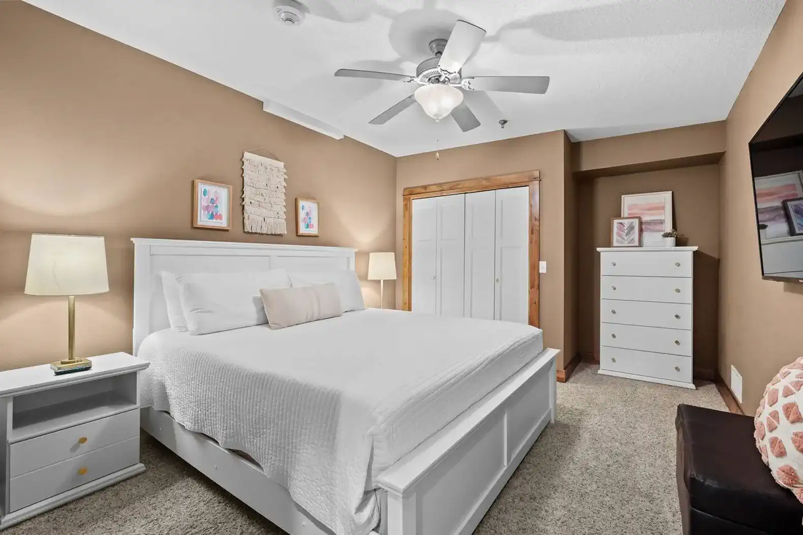 The bedroom with king sized bed, ceiling fan, closet, dresser as well as a 55" smart TV.