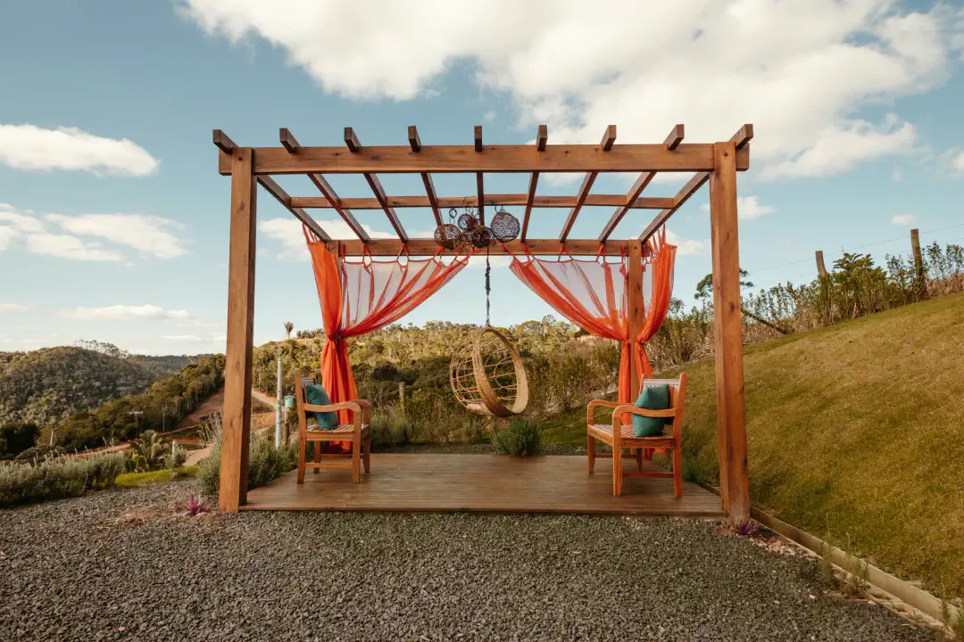 Cozy outdoor seating area with a hanging chair and draped curtains, surrounded by lush greenery and scenic views