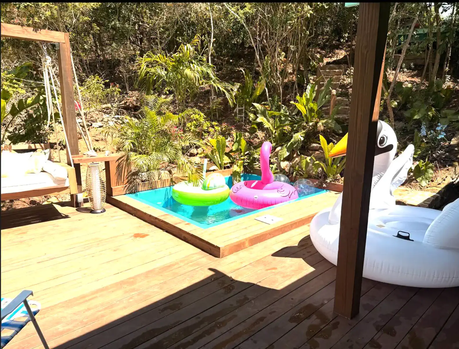 Colorful inflatable pool floats beside a small pool surrounded by lush greenery
