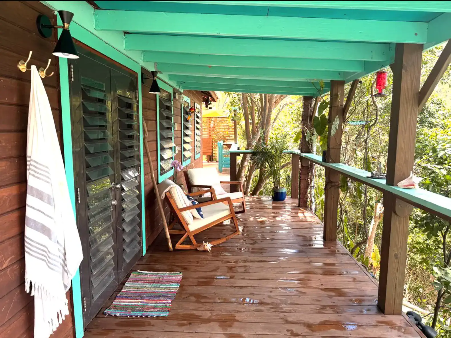 Spacious wooden deck with turquoise beams and seating surrounded by lush greenery