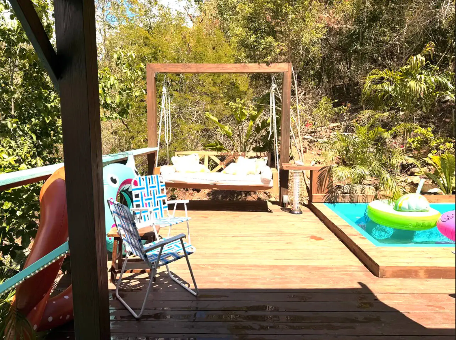Wooden deck with swing, colorful pool floats, and lounge chairs surrounded by greenery