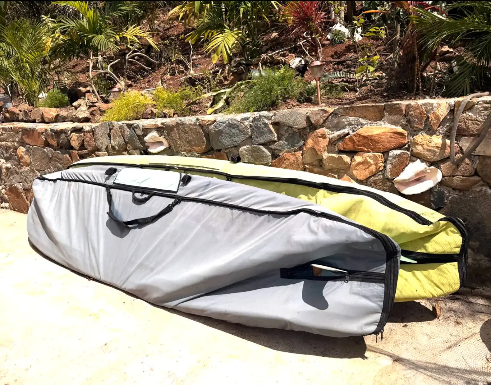 Surfboard bag resting against a stone wall surrounded by tropical plants