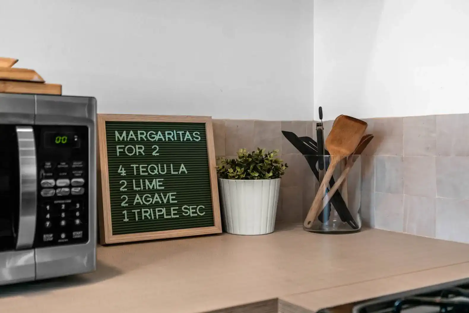 Kitchen countertop with a recipe board for margaritas, utensils, and a small plant