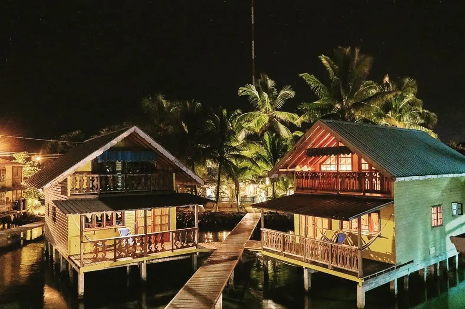 Two colorful wooden houses on stilts surrounded by palm trees at night