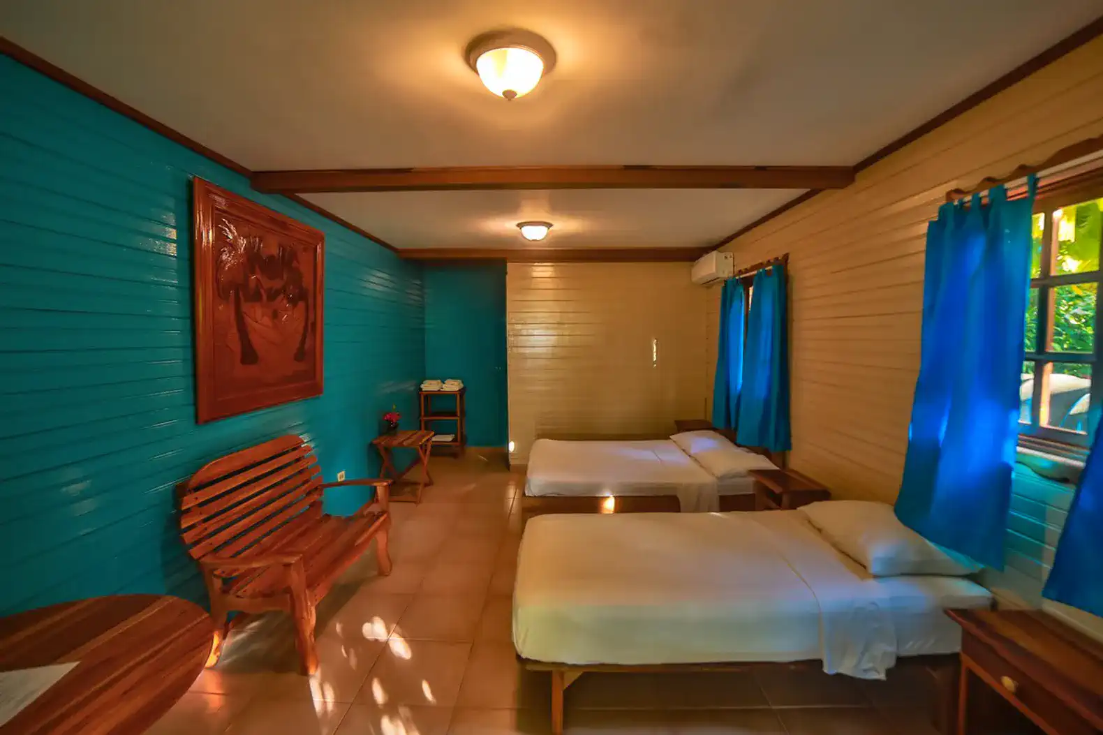 Brightly colored room with two beds, wooden furniture, and large windows
