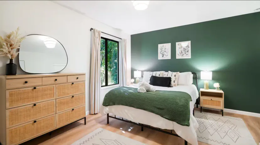 Gemütliches Hauptschlafzimmer mit grünem Akzentwand, großem Fenster und stilvollen Möbeln