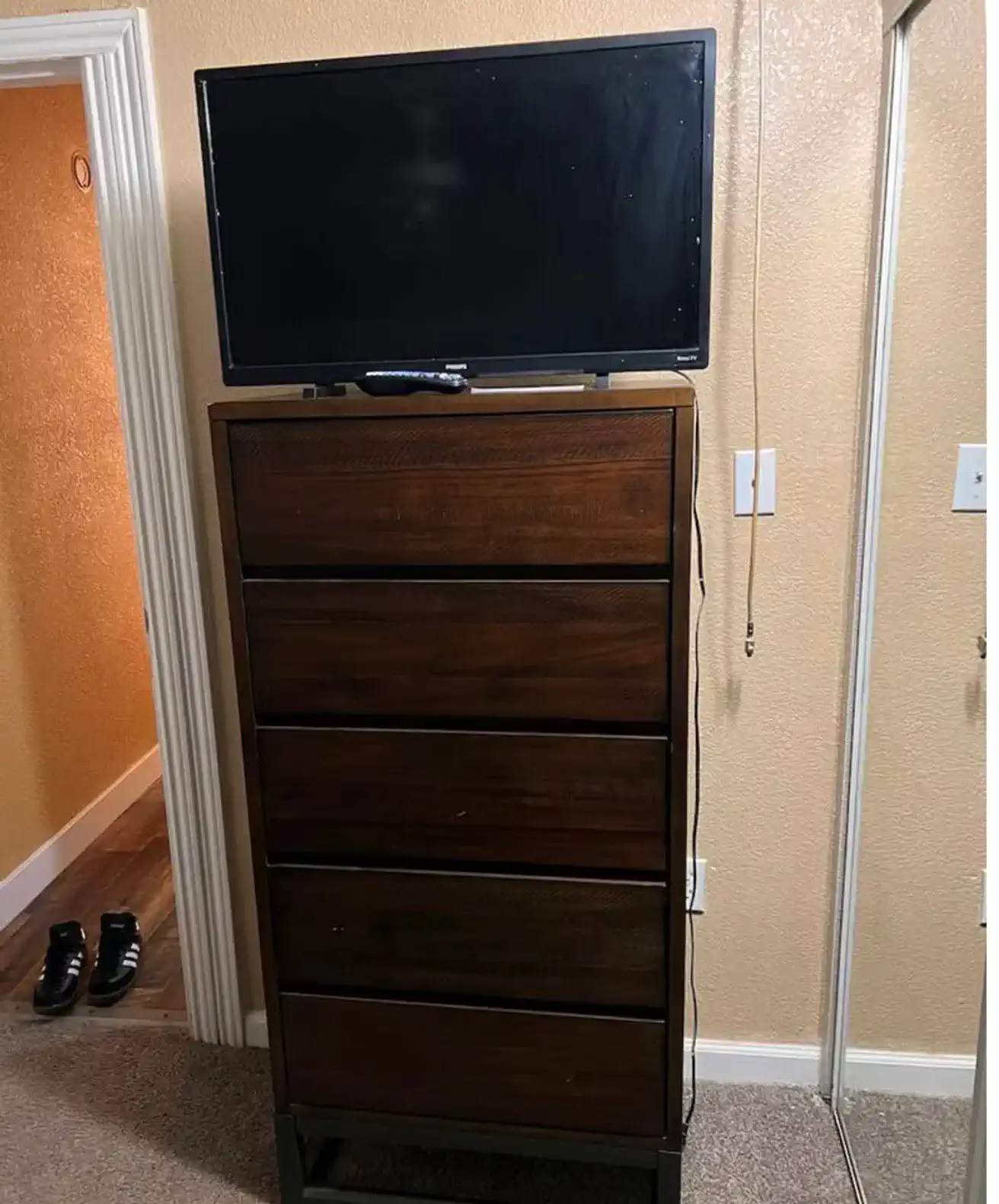 Tall dresser with a TV on top in a room with a mirror and doorway
