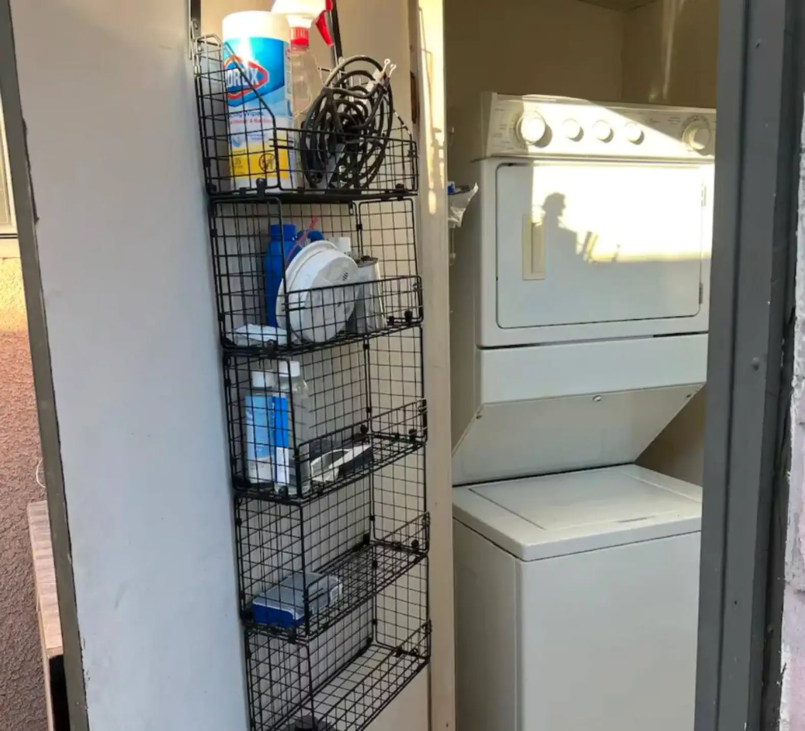 Laundry area with stacked washer and dryer and storage rack for cleaning supplies