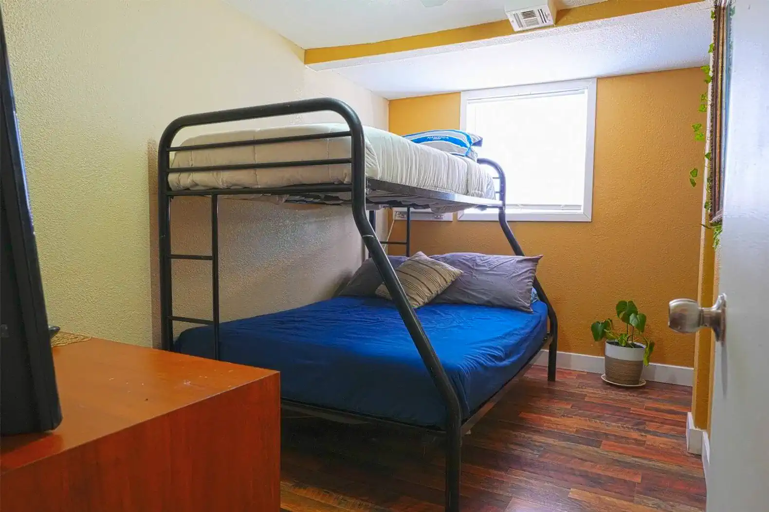 Cozy bunk room with a lower double bed and upper twin bunk, featuring a window and wooden flooring