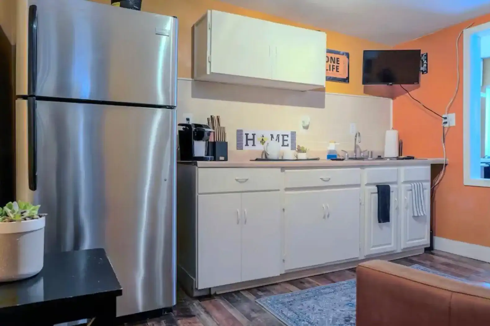 Compact kitchen with stainless steel appliances and orange accent wall