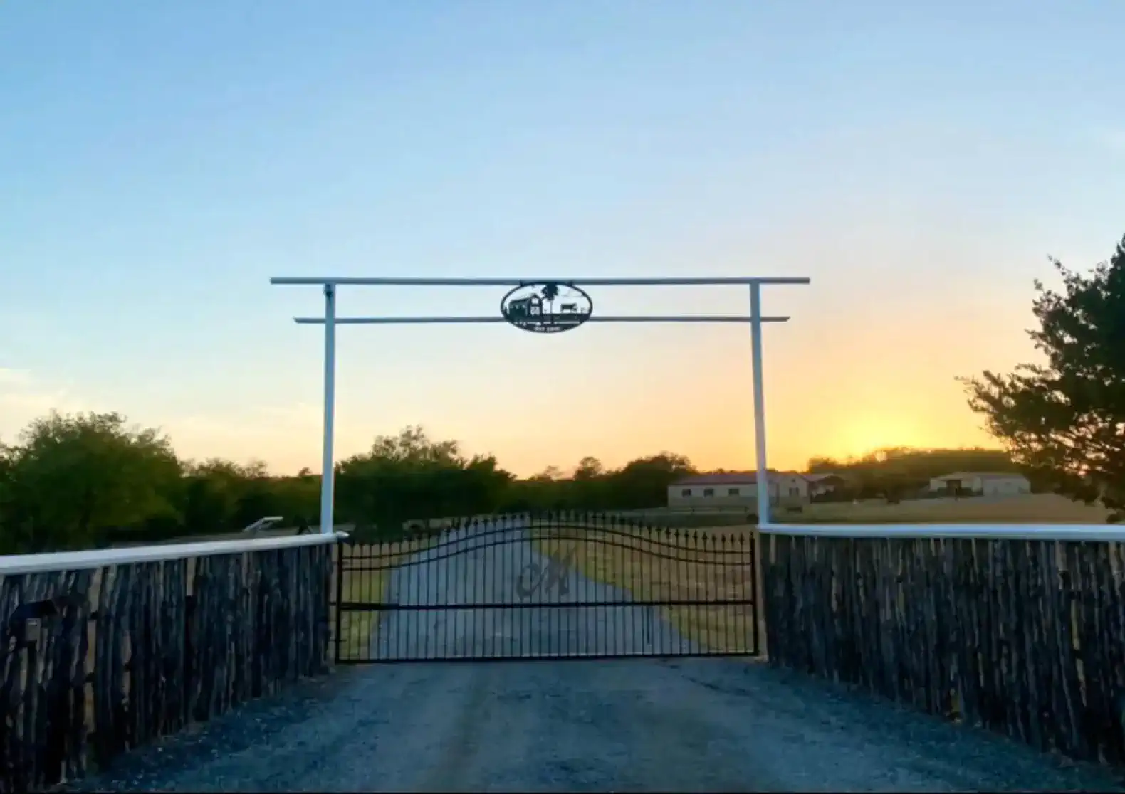 Rustic entrance gate leading to a scenic driveway at sunset