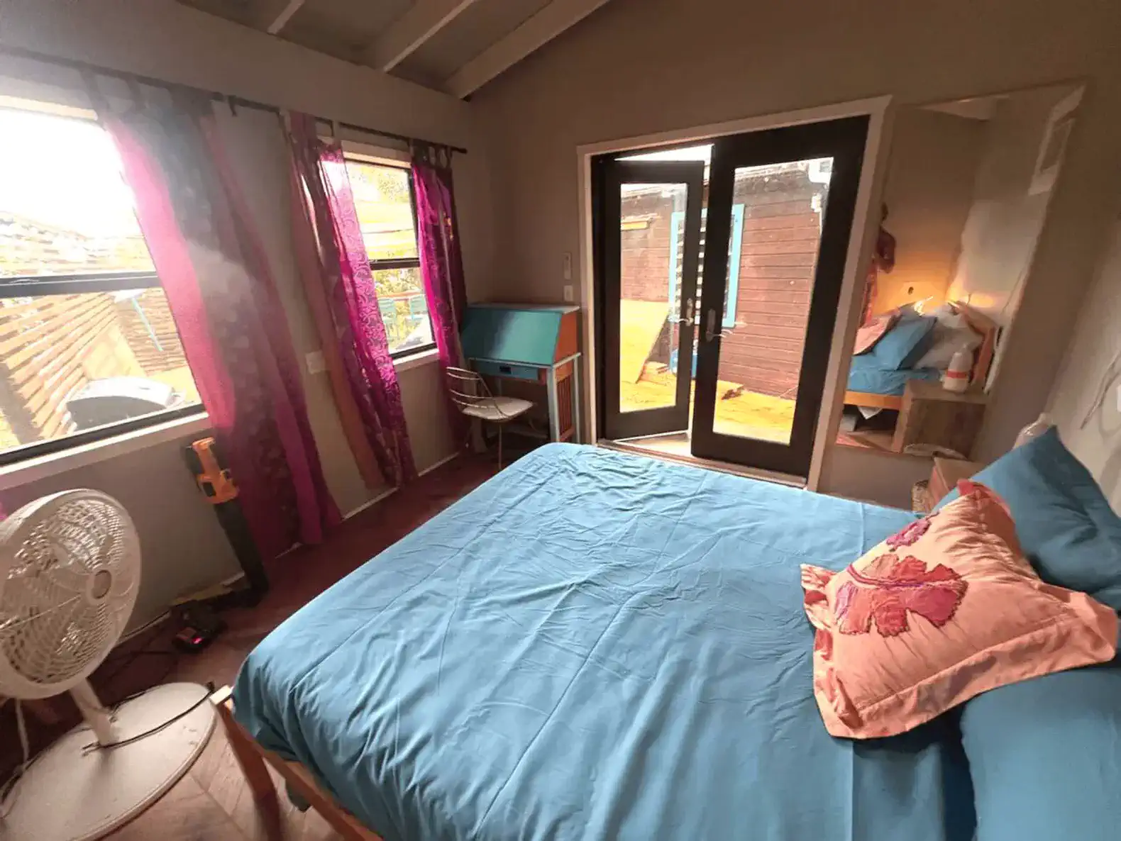 Cozy bedroom with blue bedding and colorful curtains, featuring a fan and access to an outdoor area