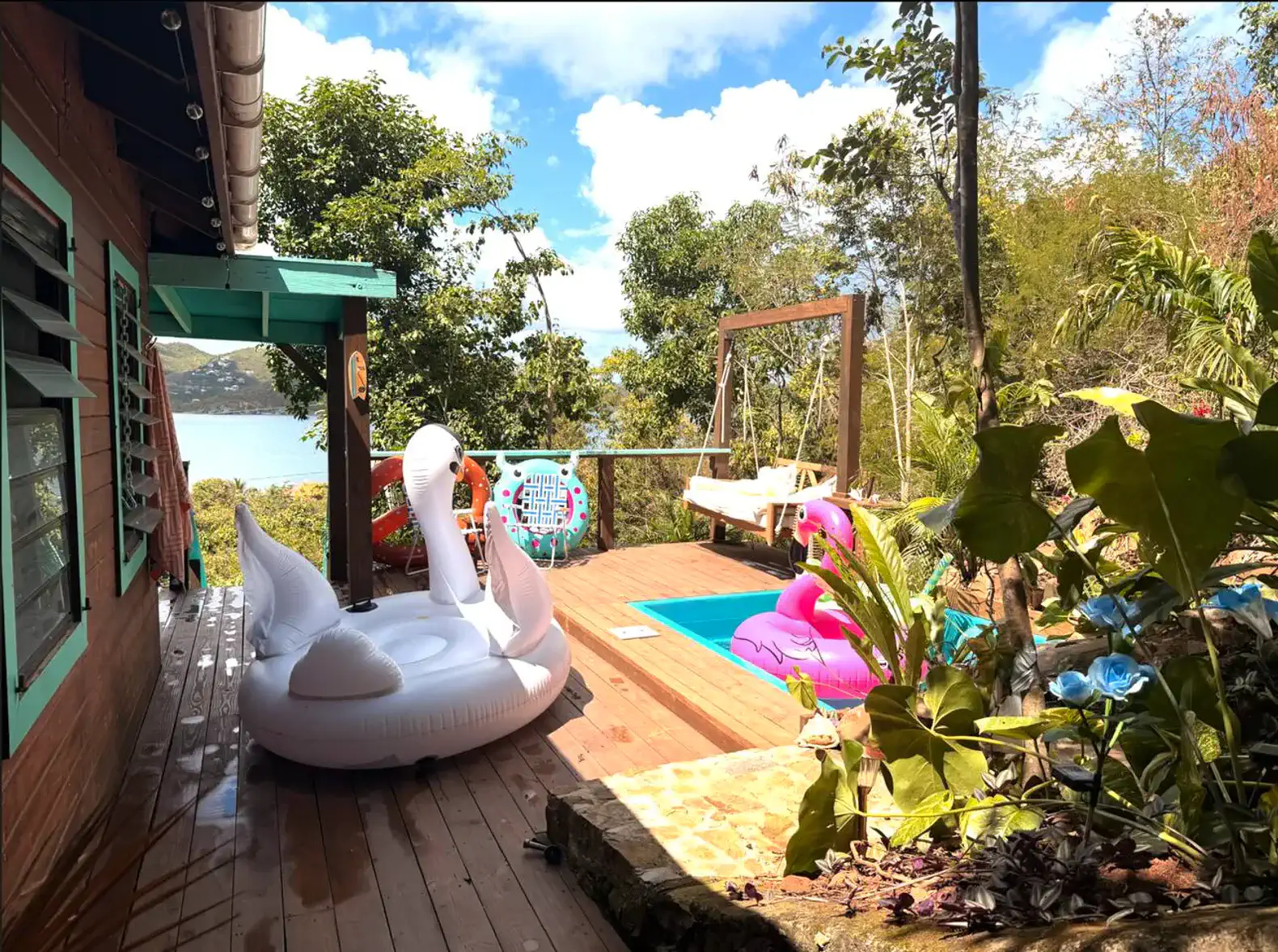 Deck com piscina e infláveis, cercado por vegetação e vista para o lago