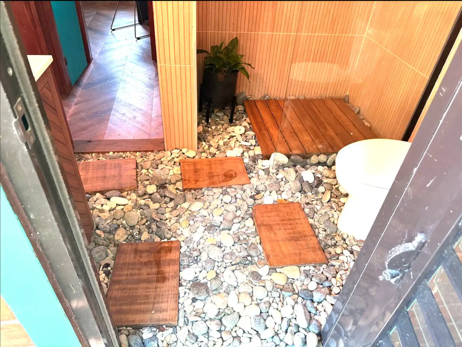 Banheiro com piso de pedras e tábuas de madeira, decoração natural e planta