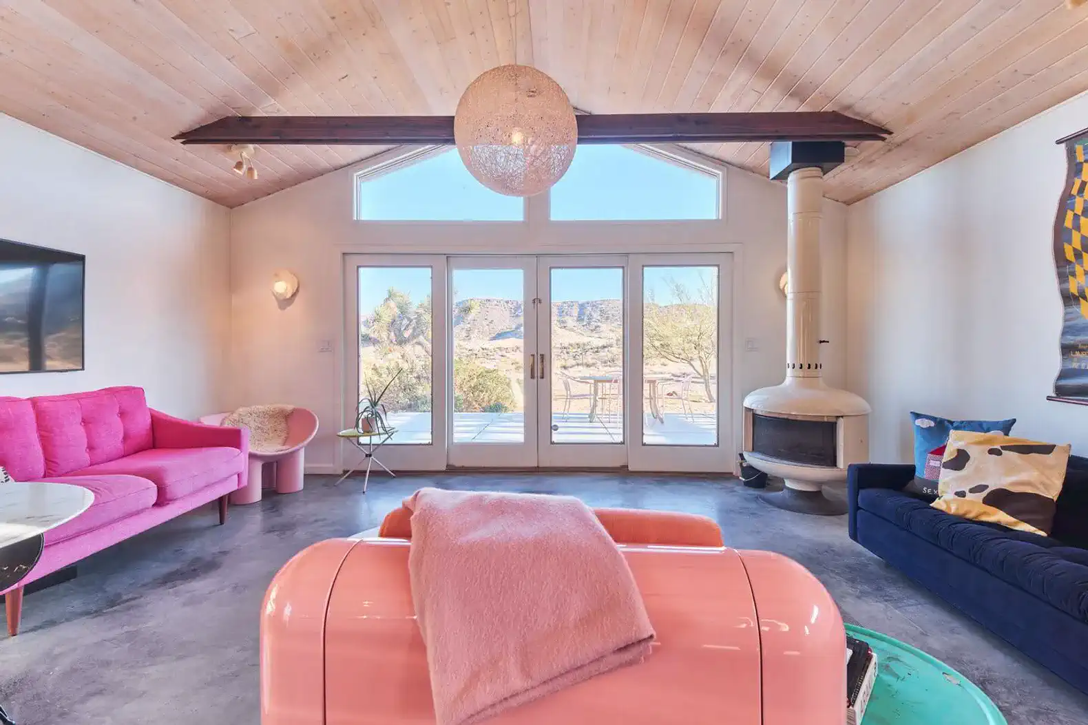 Bright living room with pink and blue sofas, large windows, and a cozy fireplace
