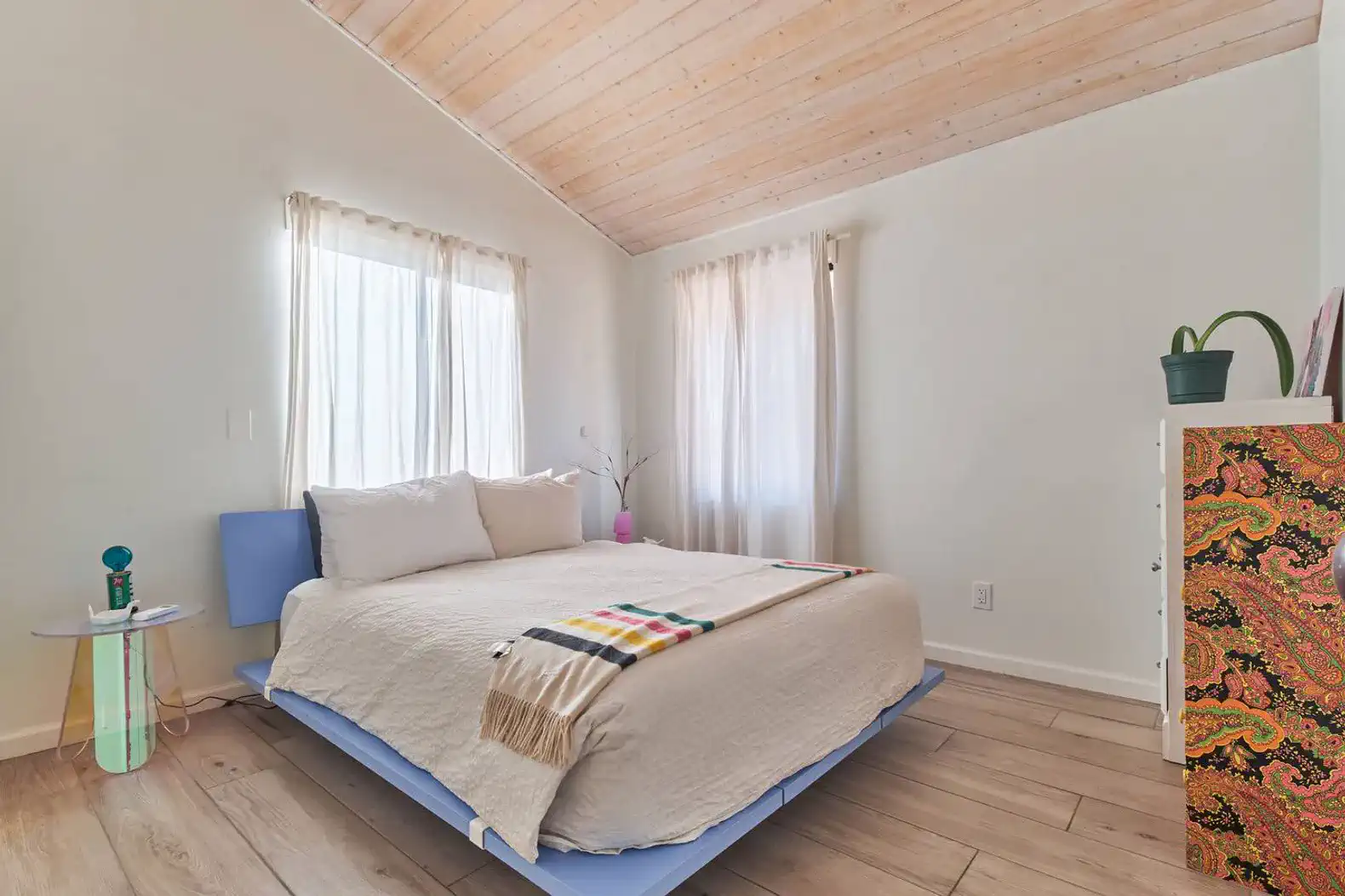 Cozy guest bedroom with a blue bed, natural light from windows, and wooden ceiling