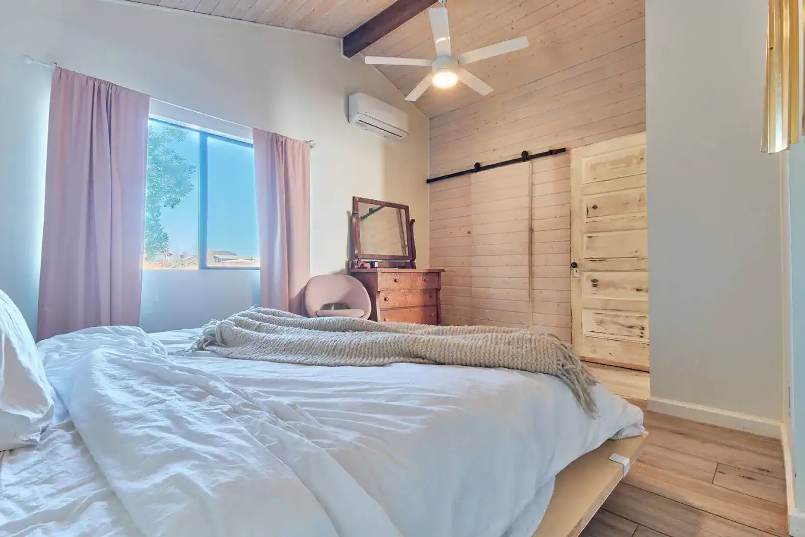 Cozy master bedroom with natural light, wooden ceiling, and soft bedding