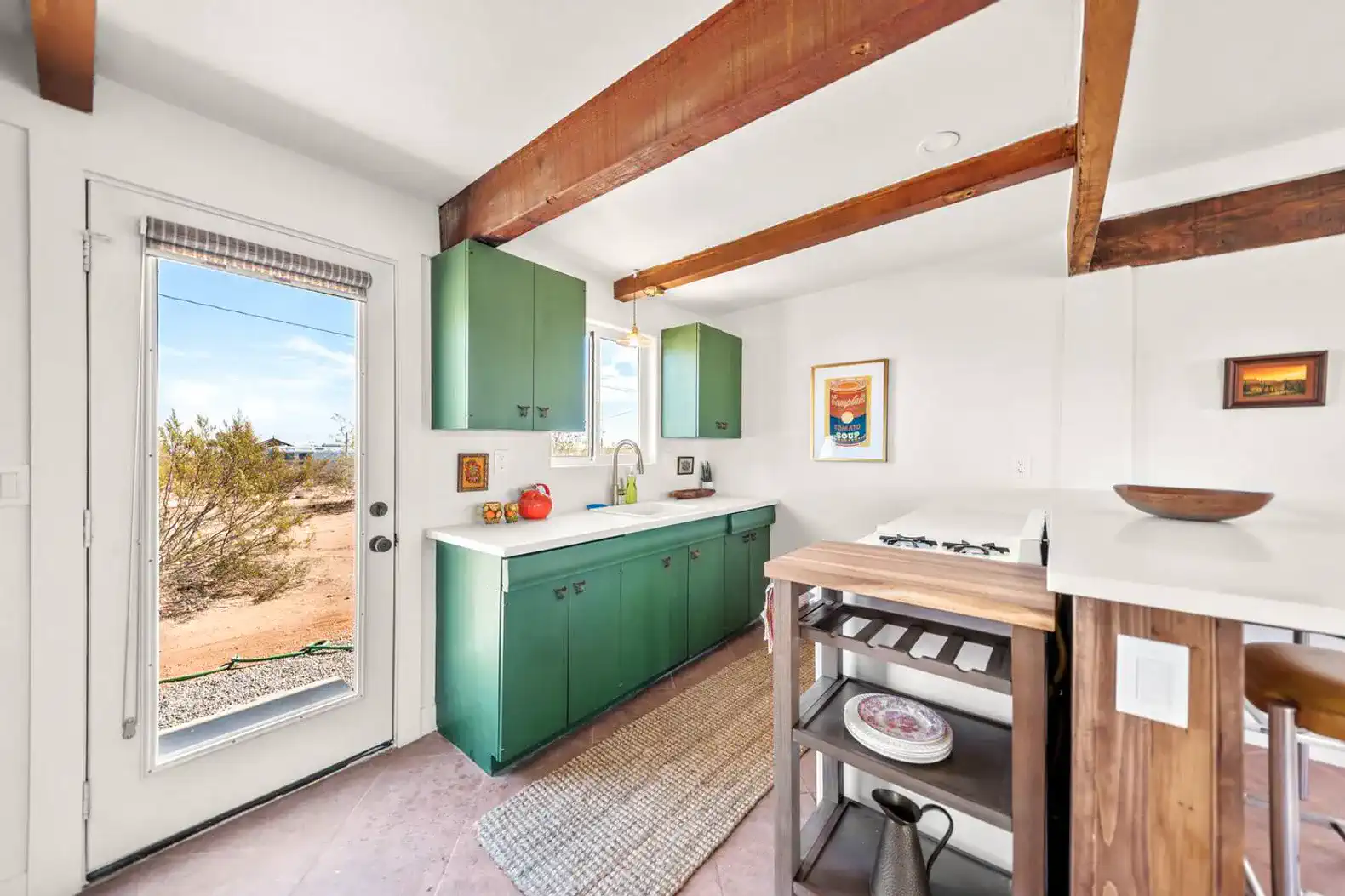 Bright kitchen with green cabinets, white countertops, and a view of the desert outside