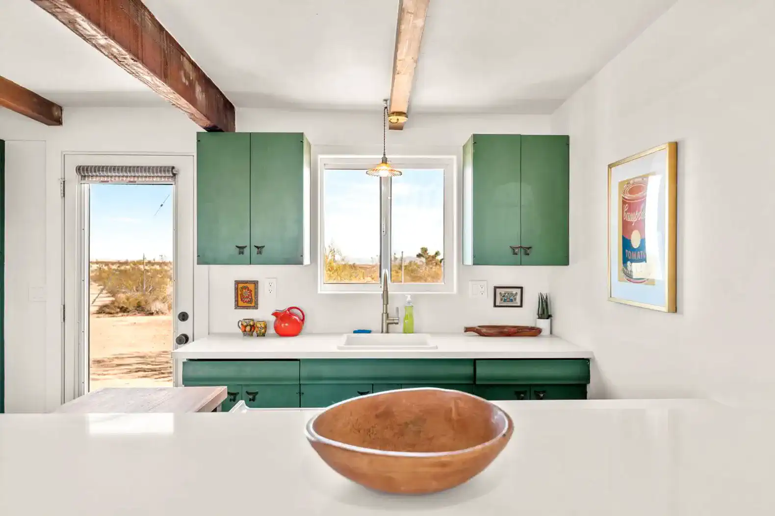 Bright kitchen with green cabinets, white countertops, and a view of the desert outside