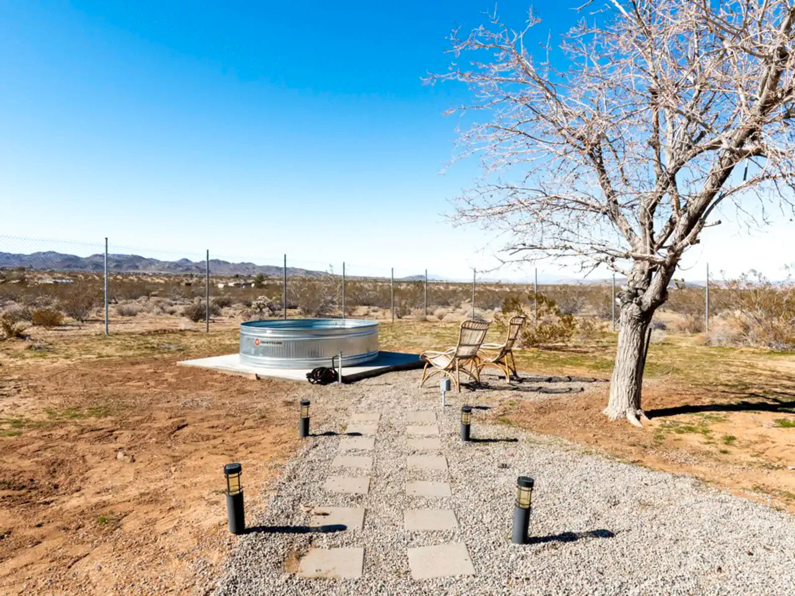 Outdoor area with a hot tub, chairs, and a pathway surrounded by desert landscape
