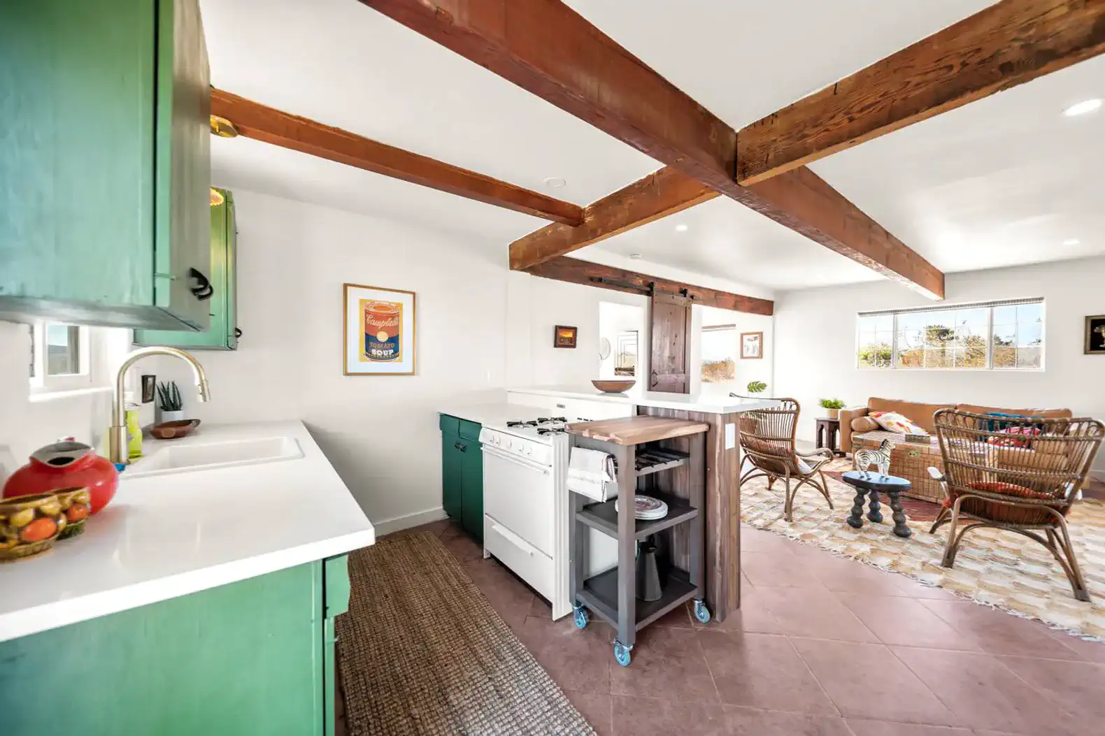 Bright kitchen with green cabinets and white countertops open to a cozy living area