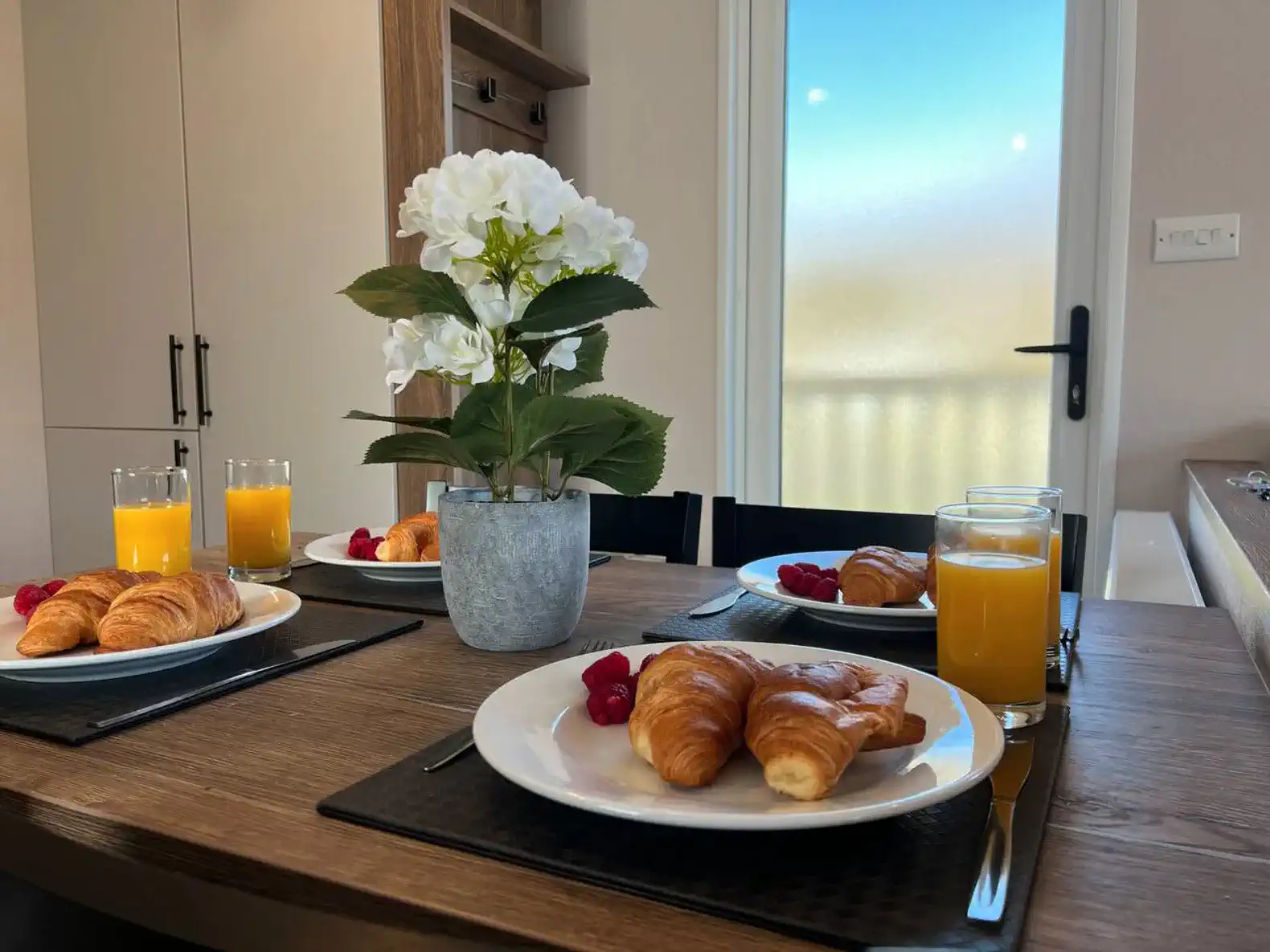 Breakfast table set with croissants, juice, and flowers in a cozy dining area
