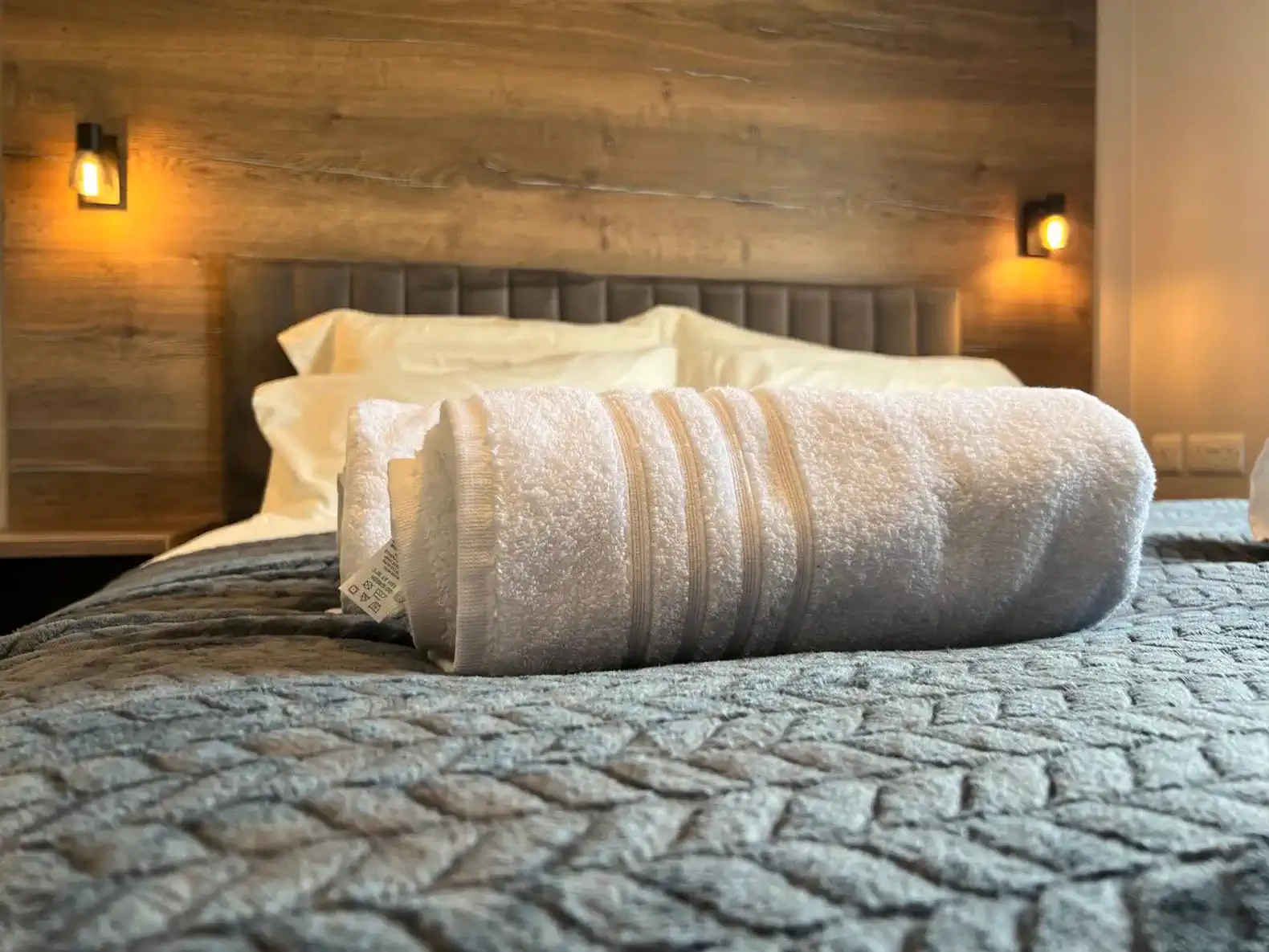 Cozy bed with neatly rolled towels on a textured blanket