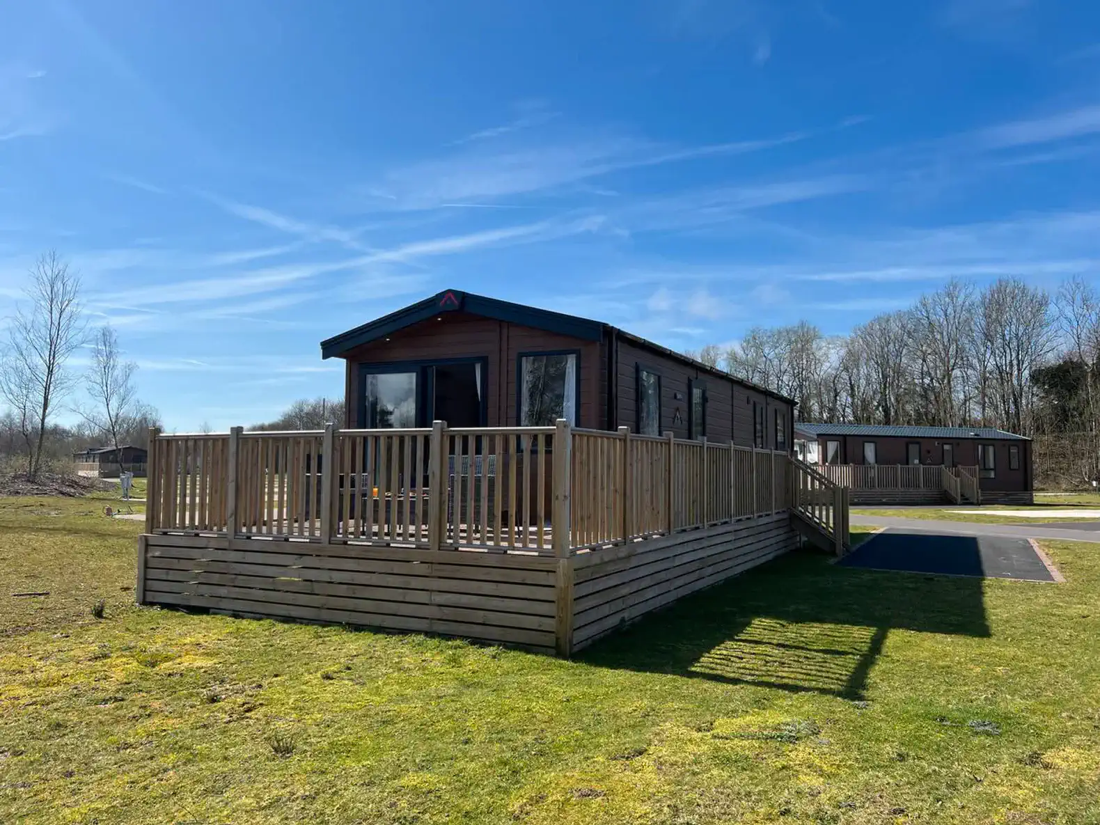 Spacious wooden deck surrounding a modern cabin with green lawn and blue sky