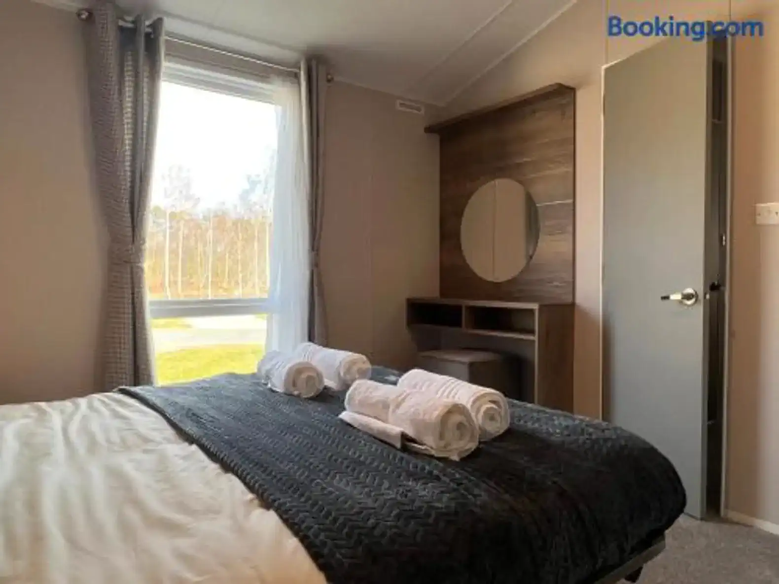 Cozy bedroom with a large window, neatly made bed, and a wooden dresser
